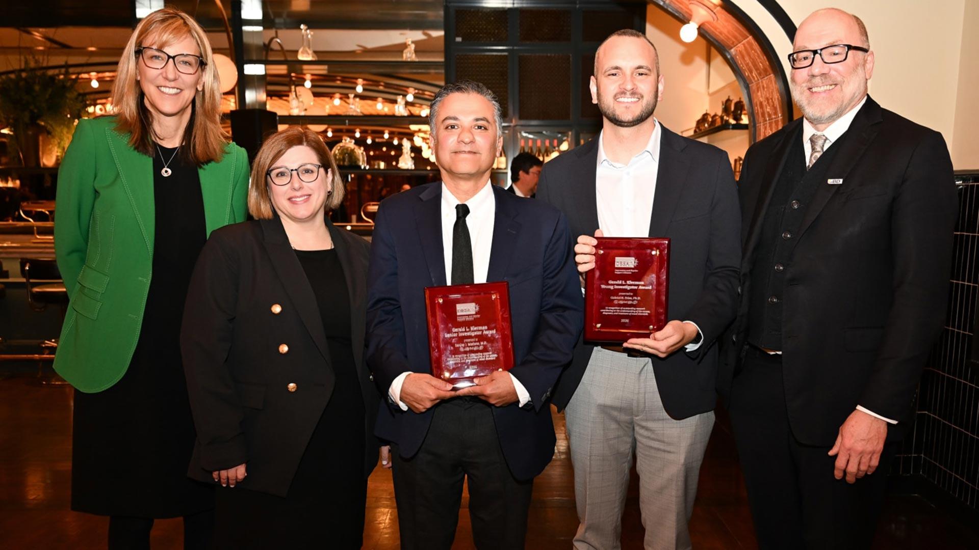 Group of award recipients and colleagues posing indoors, with two people holding Klerman Young Investigator Award plaques