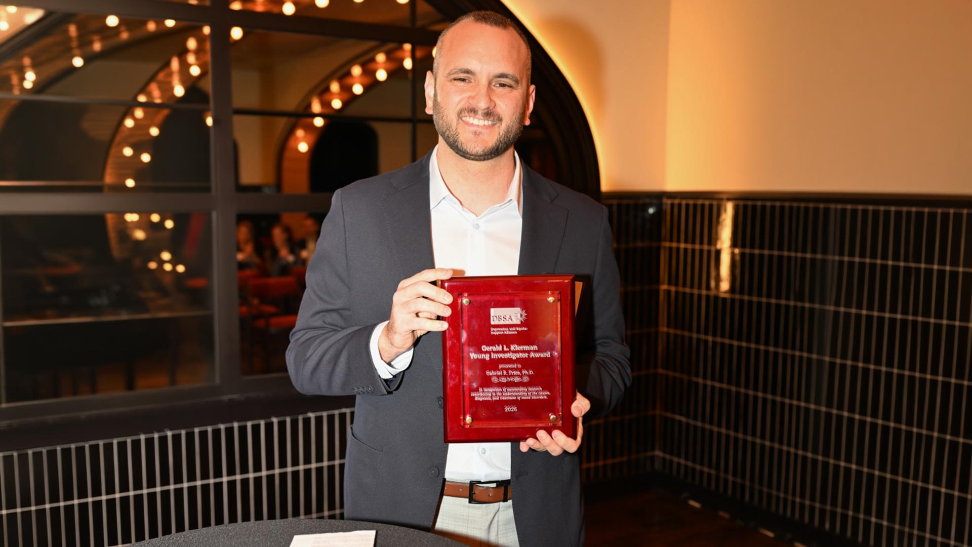 Gabriel R. Fries, PhD smiling while holding the 2026 Klerman Young Investigator Award plaque at an indoor event